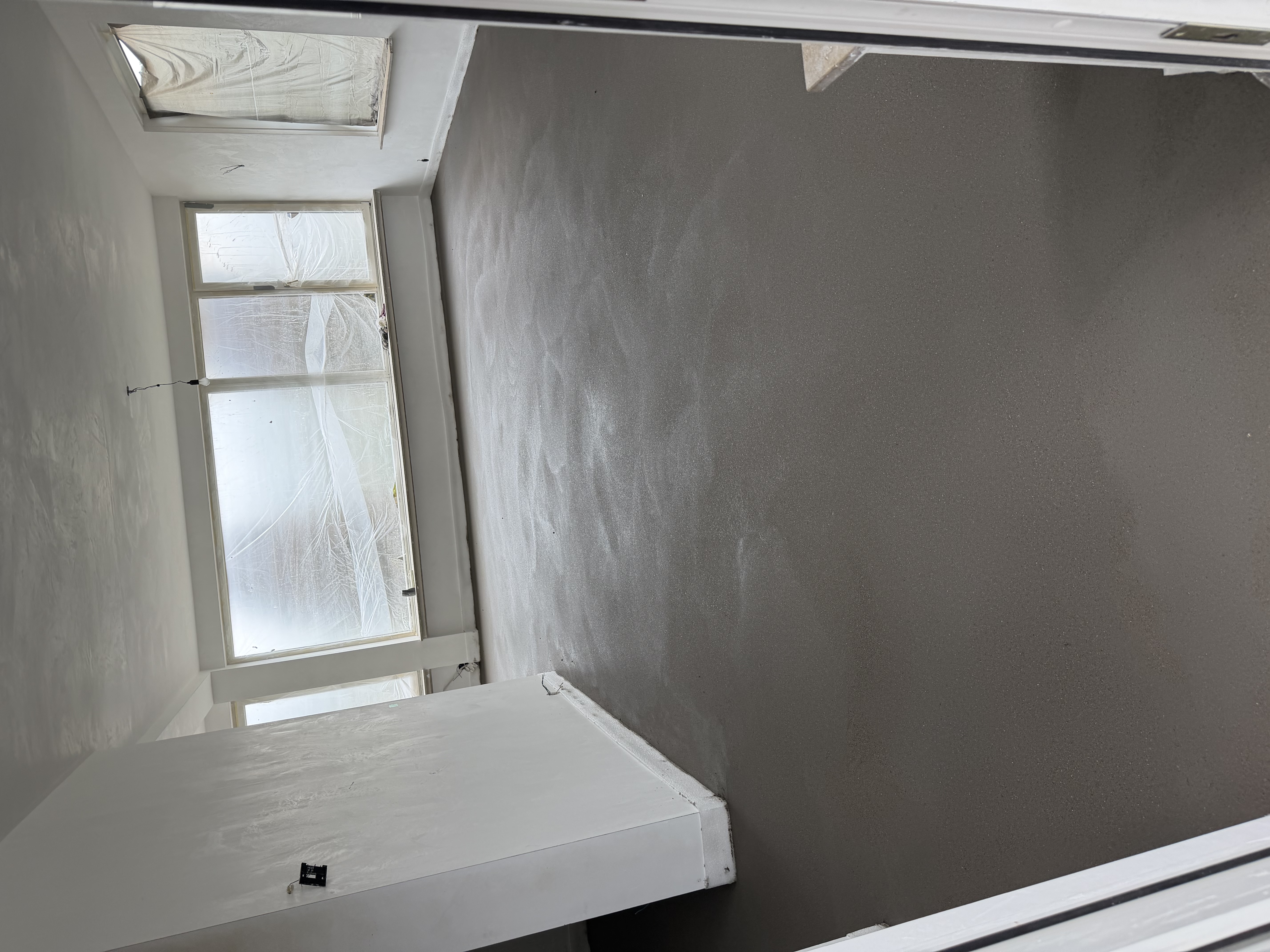 Een aangebrachte cementdekvloer in een woning met afgeplakte ramen